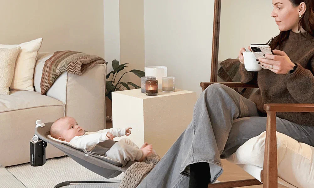 Mom enjoying a cup of coffee while Sleepytroll rocks her baby in a bouncer