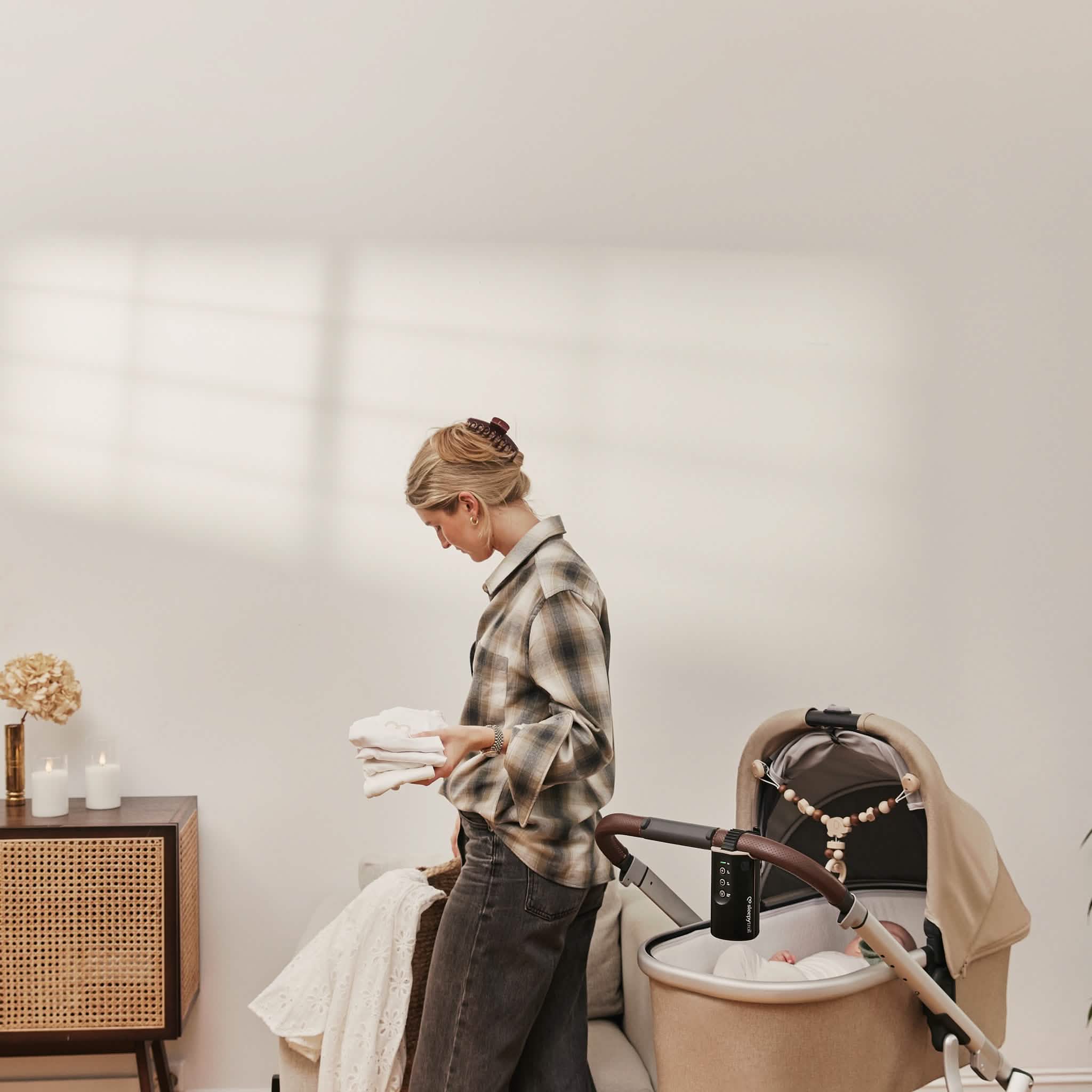 Woman in plaid shirt with baby in stroller in a room.